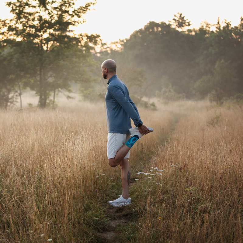 Man stretches at sunrise on a meadow with a high grass
