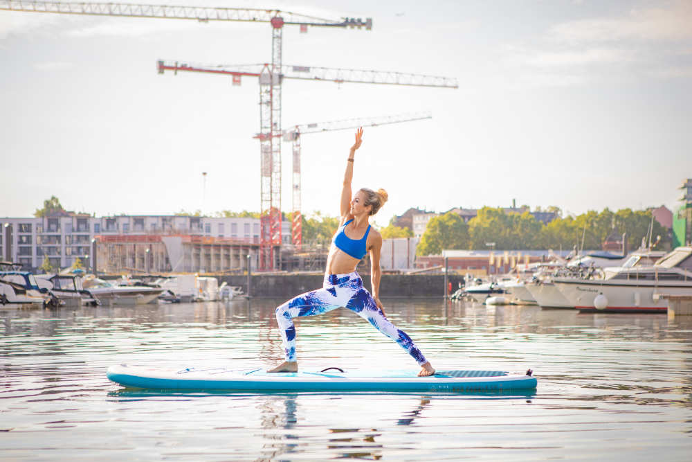 Woman makes yoga on a board with port in the background